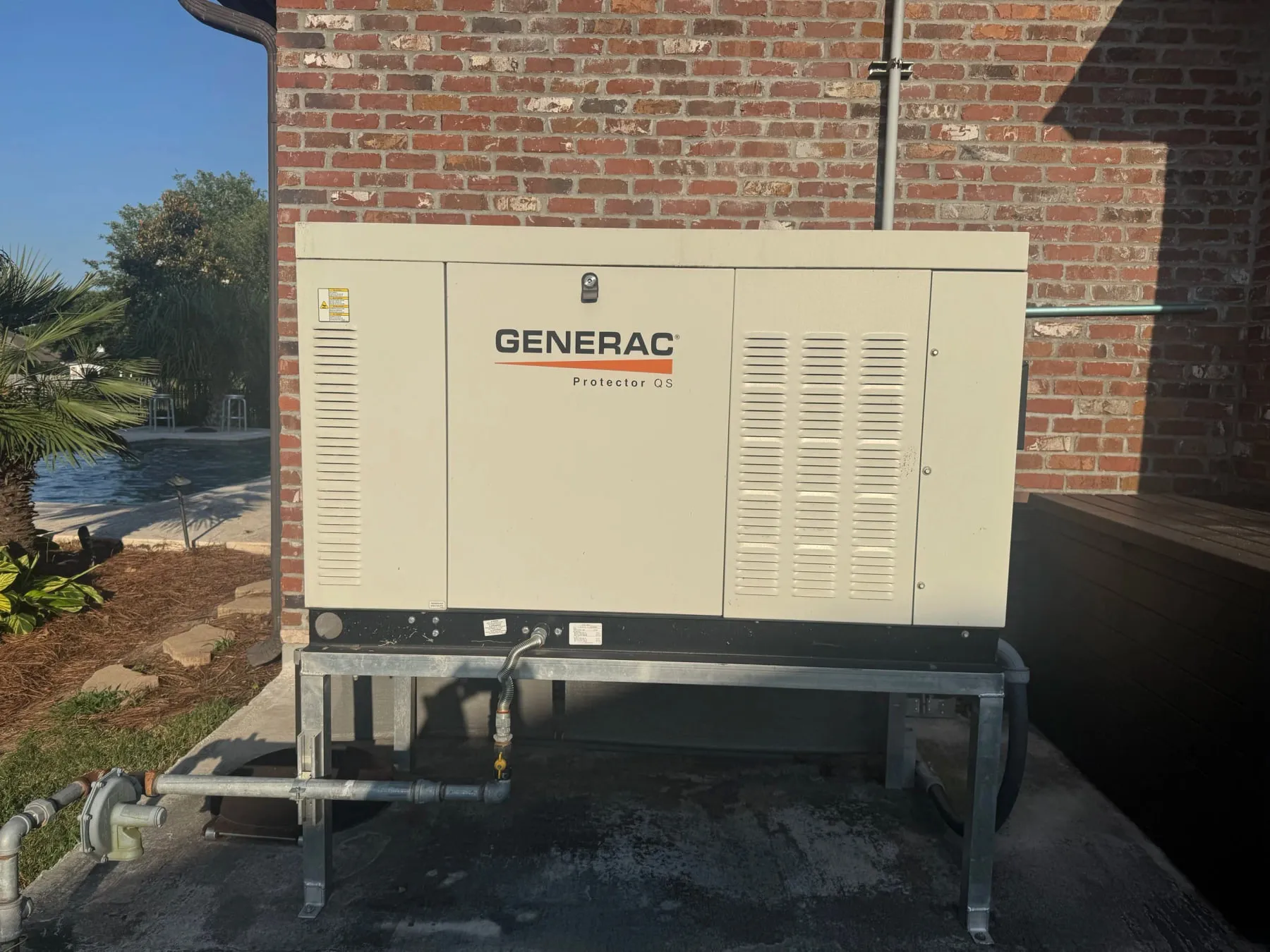 A Generac Protector QS standby generator installed on a pad beside a brick home.